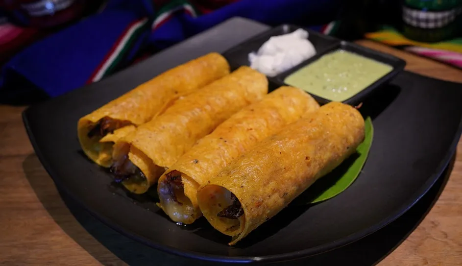 Four crispy rolled taquitos with sour cream and green salsa